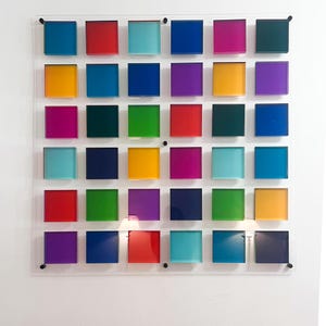 May include: A vibrant wall art piece with 30 square blocks in a grid arrangement. The blocks are in shades of blue, red, green, yellow, and purple, mounted on a clear acrylic panel. This abstract artwork is a modern design for home decor.