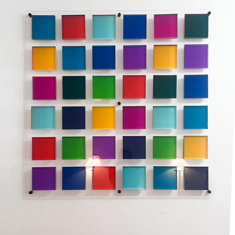 May include: A vibrant wall art piece with 30 square blocks in a grid arrangement. The blocks are in shades of blue, red, green, yellow, and purple, mounted on a clear acrylic panel. This abstract artwork is a modern design for home decor.