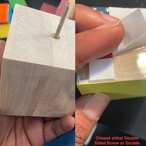 May include: A wooden cube with a screw in the center. The cube has a yellow, red, white, and blue design on one side. The text "Choose either Double Sided Screw or Double Sided Tape for fixing on wall" is written below the cube.
