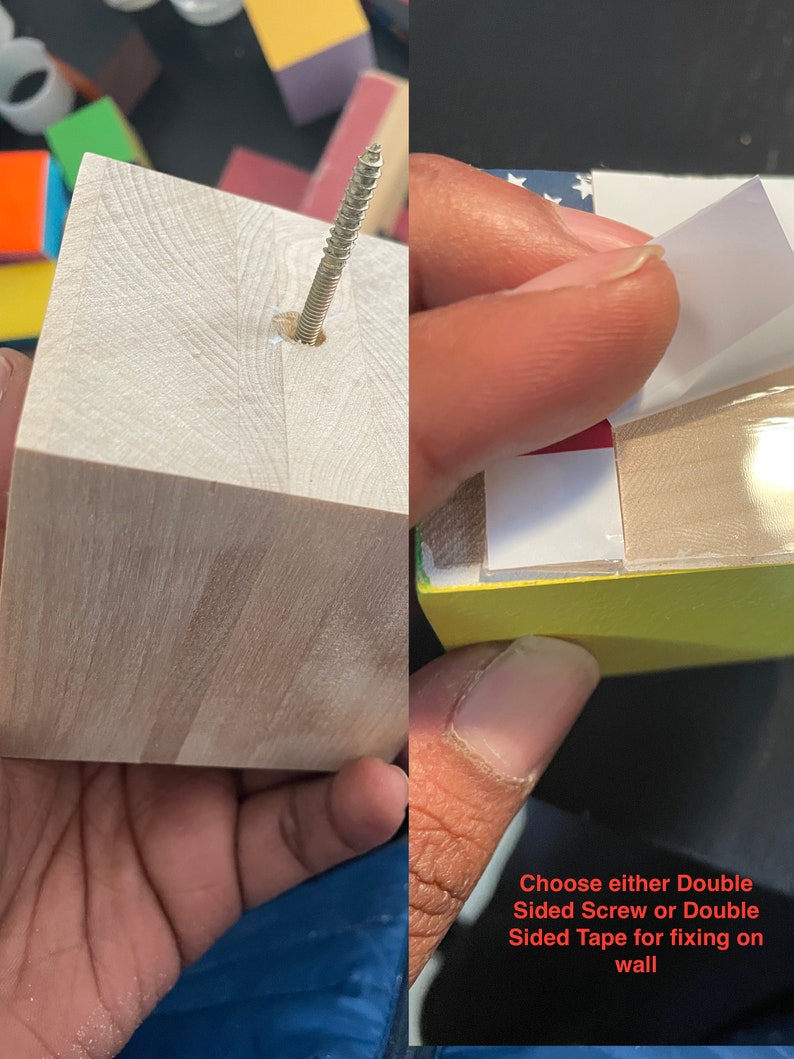 May include: A wooden cube with a screw in the center. The cube has a yellow, red, white, and blue design on one side. The text "Choose either Double Sided Screw or Double Sided Tape for fixing on wall" is written below the cube.