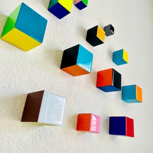 May include: A wall art installation featuring 12 colorful, geometric, wooden cubes in various sizes and colors, including yellow, blue, green, orange, pink, red, black, and white.