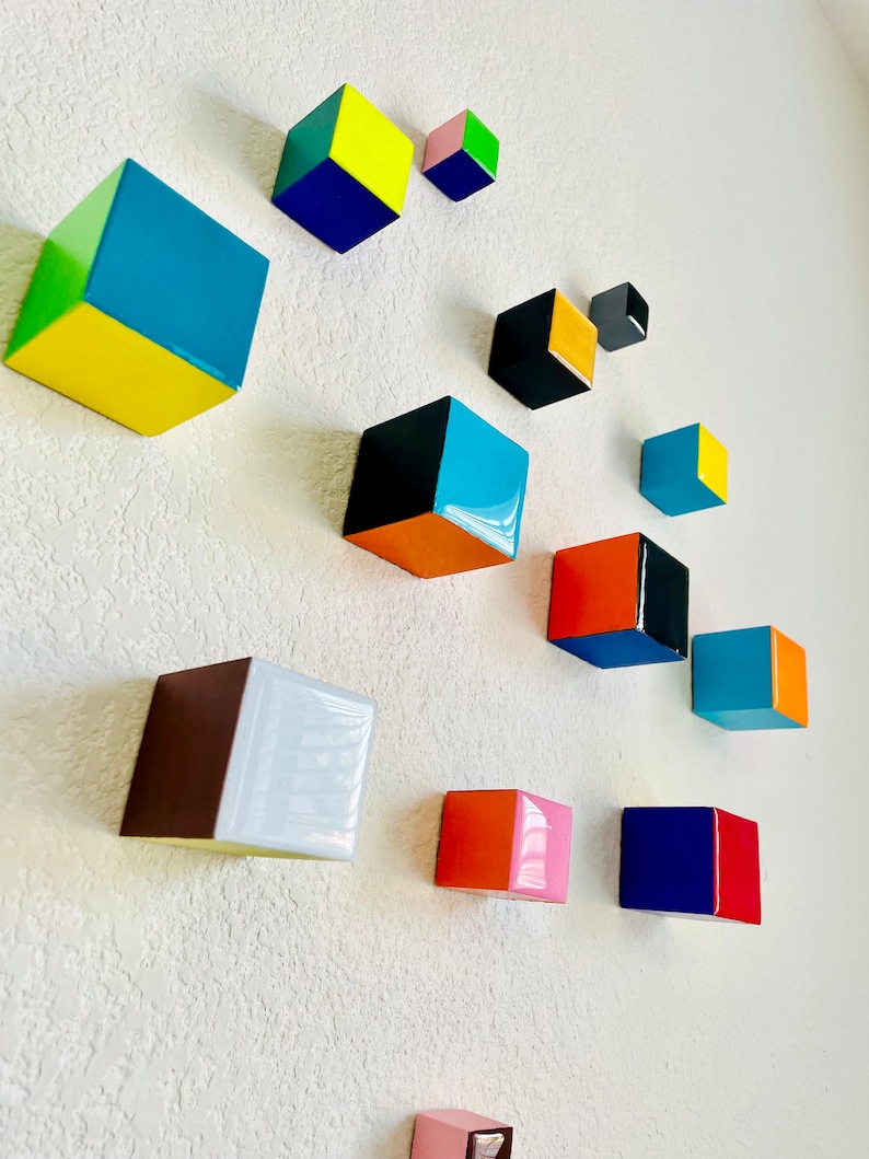 May include: A wall art installation featuring 12 colorful, geometric, wooden cubes in various sizes and colors, including yellow, blue, green, orange, pink, red, black, and white.