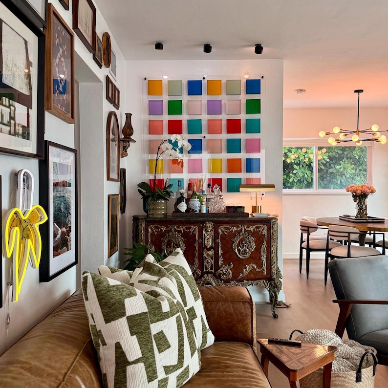 May include: A living room featuring a brown leather sofa, patterned cushions, and a vintage wooden cabinet. A colourful grid of squares adorns the wall. A neon banana art piece is on the wall.