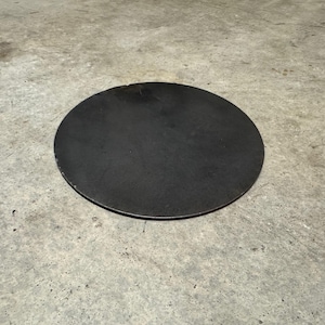 May include: A round, black metal disc. The disc is smooth and has a slightly rough texture.