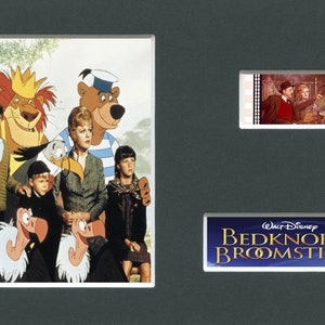 Op de afbeelding: Een ingelijste print met drie afbeeldingen. De grootste afbeelding is een kleurrijke illustratie met personages uit de film "Bedknobs and Broomsticks". Rechtsboven een filmstrook met een scène uit de film. Onderaan de titel van de film.