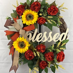 May include: A fall-themed wreath with sunflowers, red peonies, and greenery. The wreath is decorated with a brown and green striped bow and a wooden sign that reads "Blessed".