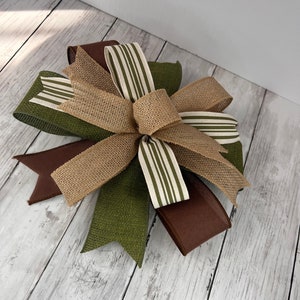 Pu&ograve; includere: Un fiocco decorativo con un mix di trame e colori. Il fiocco incorpora juta, nastri marroni e verde oliva, insieme a nastri con strisce bianche e verde oliva. Adatto a vari progetti di artigianato e decorazione.