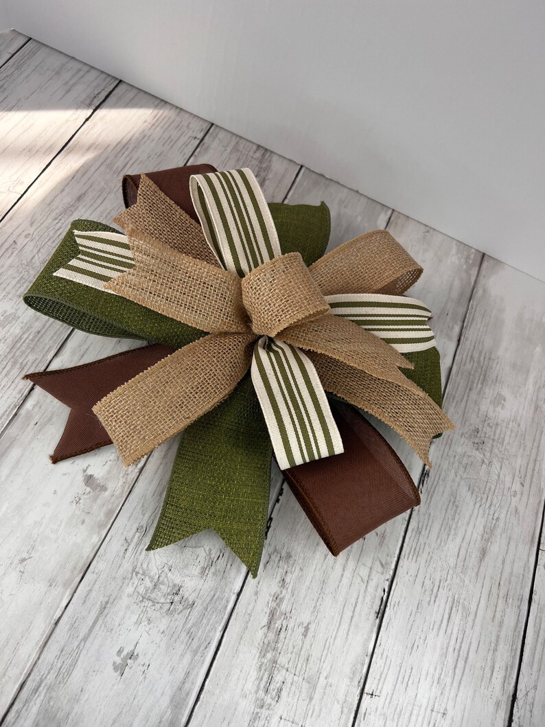 Pu&ograve; includere: Un fiocco decorativo con un mix di trame e colori. Il fiocco incorpora juta, nastri marroni e verde oliva, insieme a nastri con strisce bianche e verde oliva. Adatto a vari progetti di artigianato e decorazione.