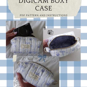 May include: A white and blue floral patterned Digicam Boxy Case with a zip closure. The case has a gold-coloured zip pull and a small label that reads "Kelsie Bird Creates". The image also includes a black digital camera.