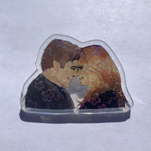 May include: A holographic sticker featuring a couple looking at each other with a floral pattern in the background.