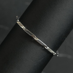 Puede incluir: Un brazalete plateado con un diseño geométrico. El brazalete está en un expositor negro.