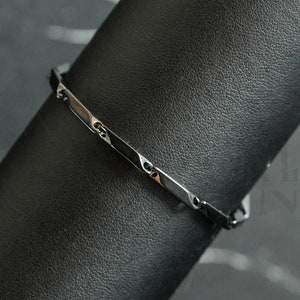 Puede incluir: Un brazalete plateado sobre un fondo negro. El brazalete tiene un diseño de eslabón de cadena.