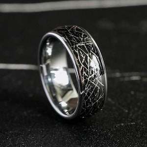 May include: A ring with a polished silver-toned interior and a dark, textured exterior featuring a complex pattern of intersecting white lines. The band has a smooth, rounded profile and a metallic finish, displaying a distinct contrast between the dark outer surface and the reflective inner band.