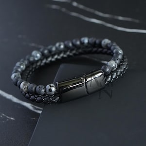 Peut inclure: Un bracelet en cuir noir avec un fermoir magnétique. Le bracelet est fait de pierres de lave noire et de perles d'agate grises.