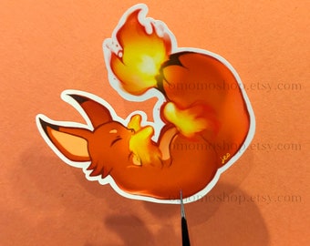 May include: A sticker of a cartoon fox with orange fur and a bright orange flame tail. The fox is curled up with its tail wrapped around its body. The sticker is on a light orange background.
