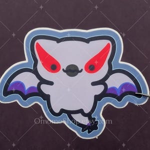 May include: A sticker of a cartoon bat with purple wings and red eyes. The bat is white with a black nose and a small black mouth.