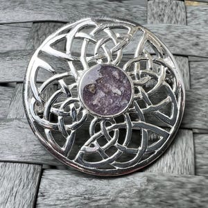 Peut inclure: Une broche celtique en argent avec un nœud celtique et une pierre violette et blanche au centre.