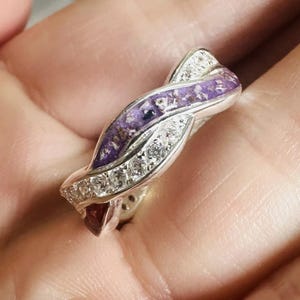 Peut inclure: Une bague en argent avec un design en spirale violet et blanc. La bague est sertie de petites pierres claires.