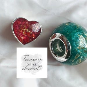 Peut inclure: Deux objets décoratifs : un objet en forme de cœur avec des accents rouges et dorés et un globe vert avec un bord argenté. Le cœur et le globe sont sur une surface blanche. Le texte "Treasure your moments" est également présent.