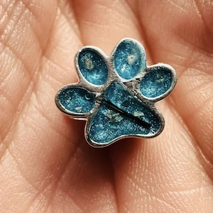 Peut inclure: Un petit charme en argent en forme de patte d'animal avec un remplissage en époxy bleu pailleté. Le charme est petit et serait parfait pour un collier ou un bracelet.
