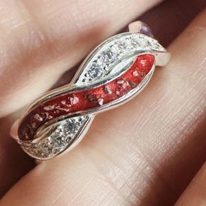 Peut inclure: Une bague en argent avec un motif en spirale rouge et blanc. La bague est sertie de petites pierres claires.
