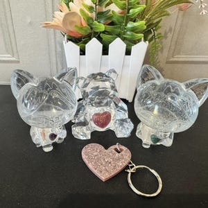 May include: Three crystal animal figurines, a bear, a dog, and a cat, with pink and green accents. A pink glitter heart keychain is in the foreground.