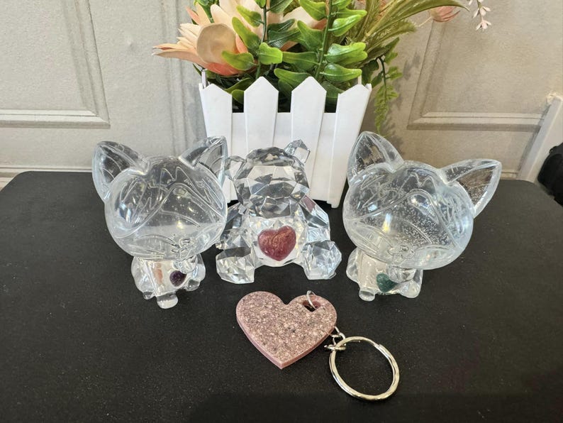 May include: Three crystal animal figurines, a bear, a dog, and a cat, with pink and green accents. A pink glitter heart keychain is in the foreground.