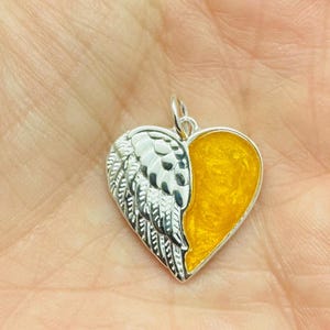 Peut inclure: Un pendentif en argent en forme de cœur avec un motif d'aile d'ange détaillé d'un côté et un remplissage en résine jaune de l'autre.