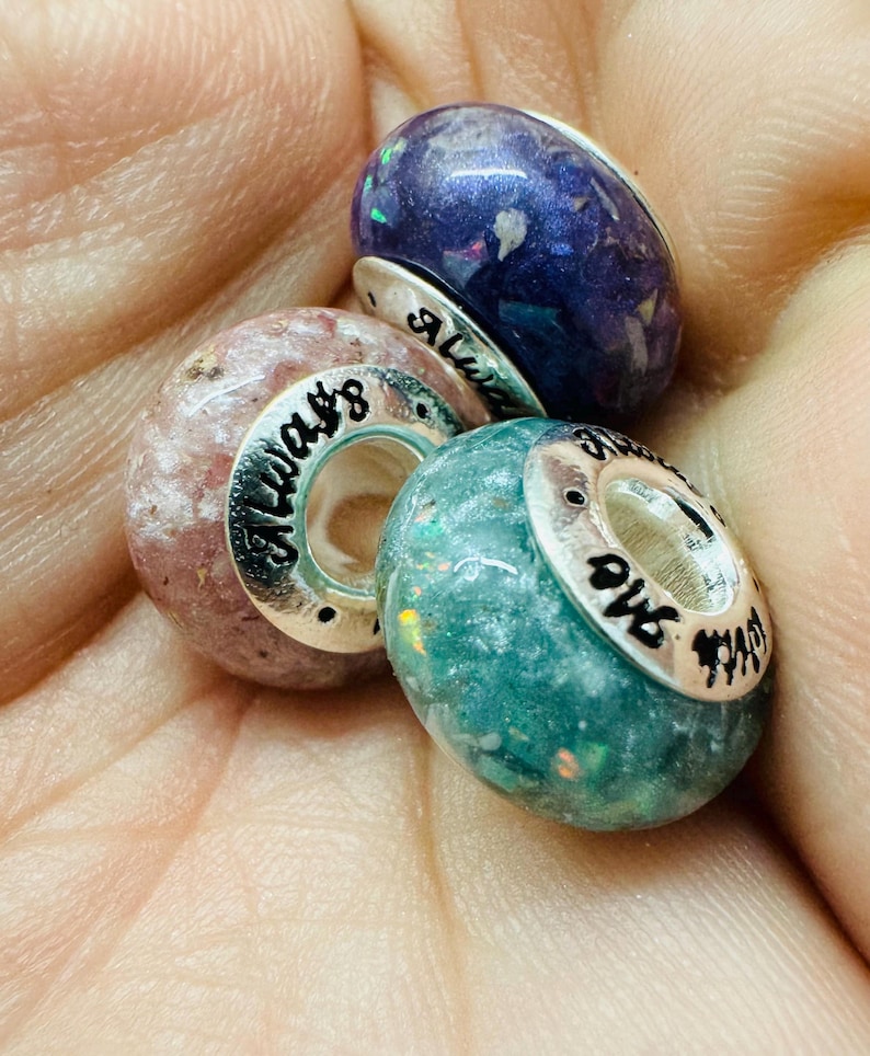 May include: Three glass beads with silver accents and inscribed text. The beads are purple, pink, and aqua  with flecks of glitter. The text on the beads reads "Always", "Love", and "And", respectively.