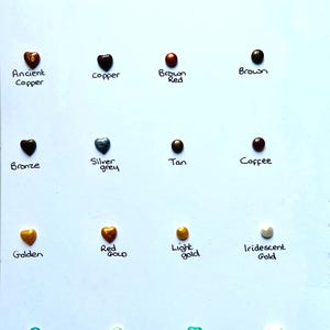 May include: A chart of 15 heart-shaped resin pieces in various colors, including mermaid pink, apricot pink, iridescent red, rose gold, ancient copper, copper, brown red, brown, bronze, silver grey, tan, coffee, golden, red gold, light gold, iridescent gold, blue green, tea green, golden green, and iridescent green.