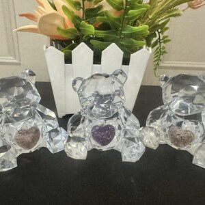 May include: Three crystal bear figurines with amethyst hearts. Each bear is clear and faceted, with a purple heart in its chest.