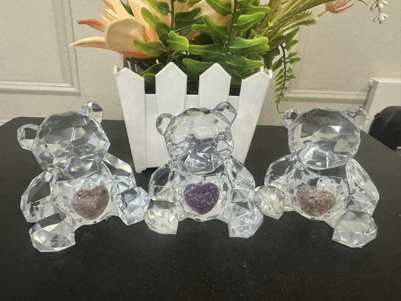 May include: Three crystal bear figurines with amethyst hearts. Each bear is clear and faceted, with a purple heart in its chest.