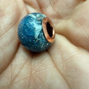 May include: A blue and white speckled round bead with a sterling silver  rose gold plated  metal ring around the top.