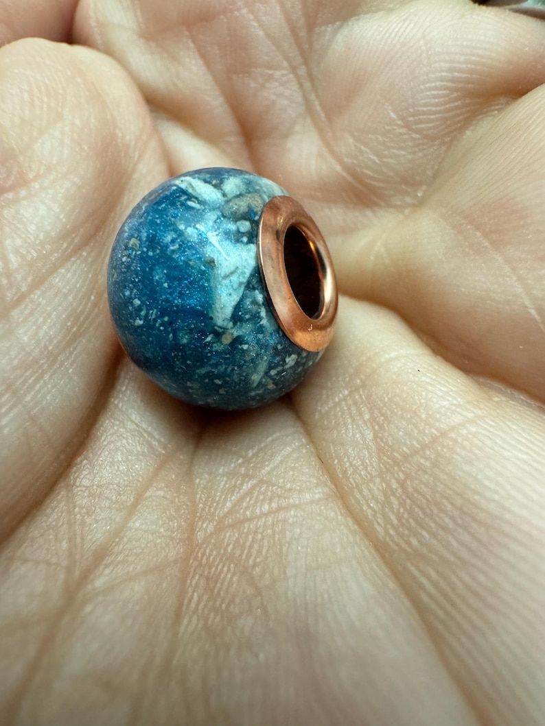 May include: A blue and white speckled round bead with a sterling silver  rose gold plated  metal ring around the top.