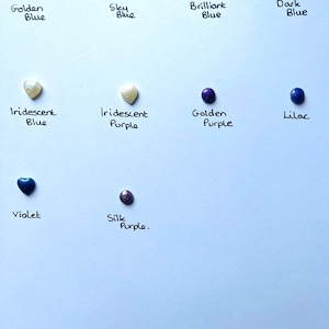 May include: Assortment of small round and heart-shaped glass beads in various shades of blue, purple, and white. The beads are labeled with their color names, including Golden Blue, Sky Blue, Brilliant Blue, Dark Blue, Iridescent Blue, Iridescent Purple, Golden Purple, Lilac, Violet, and Silk Purple.