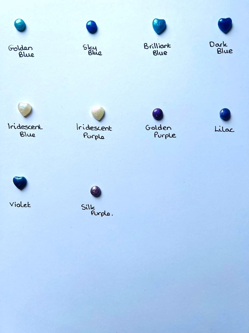 May include: Assortment of small round and heart-shaped glass beads in various shades of blue, purple, and white. The beads are labeled with their color names, including Golden Blue, Sky Blue, Brilliant Blue, Dark Blue, Iridescent Blue, Iridescent Purple, Golden Purple, Lilac, Violet, and Silk Purple.