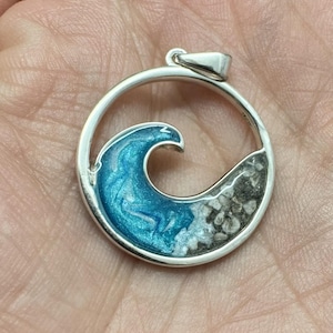 May include: A silver circle pendant with a blue wave and white sand inside. The wave is made of resin and the sand is real.