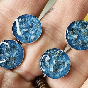 May include: Four round resin cabochons with a blue background and white and gold flecks. The cabochons are set in silver settings.