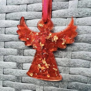 Peut inclure: Ornement d'ange en verre rouge avec des paillettes dorées et un ruban rouge pour l'accrocher.