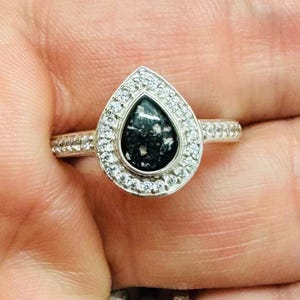 Peut inclure: Une bague en argent avec une pierre noire en forme de larme entourée de pierres de zircone cubique transparentes.