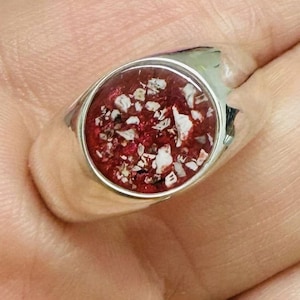 Peut inclure: Une bague en argent avec une pierre ovale rouge et blanche. La pierre est remplie de petites taches blanches.