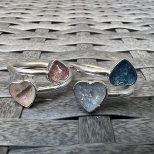 Peut inclure: Trois bagues en argent avec des breloques en forme de cœur. Les breloques sont remplies de paillettes et sont disponibles en rose, bleu et blanc.