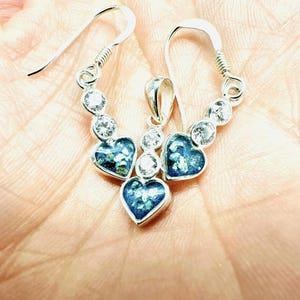 Peut inclure: Un collier pendentif en argent et des boucles d'oreilles assorties avec un groupe de trois cœurs bleus et des pierres de zircone cubique claires.