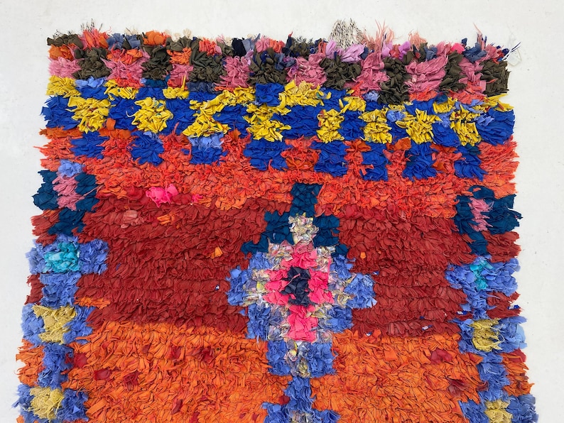 The image is a vibrant, colorful textile with a variety of hues, including red, blue, yellow, and orange. The textile appears to be a rug or a large woven piece, with intricate patterns and designs. The image is not a single, continuous scene but rather a collection of individual images that come together to create a larger, visually striking composition.