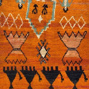 a vibrant, intricately designed rug with a striking orange and black color scheme. The rug is adorned with various geometric patterns and shapes, including triangles, diamonds, and other abstract designs. The rug appears to be a traditional or cultural textile, showcasing the craftsmanship and artistry of the creator.