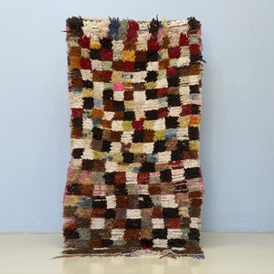 Peut inclure: Un tapis rectangulaire tissé à la main avec un motif à carreaux. Le tapis présente une variété de couleurs, dont le blanc, le marron, le rouge, le jaune et le rose. Le tapis a une texture touffue et est probablement en laine.