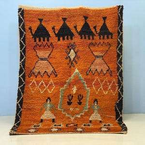 a vibrant, intricately designed rug with a striking orange and black color scheme. The rug is adorned with various geometric patterns and figures, including people and animals, creating a visually captivating and culturally rich design.