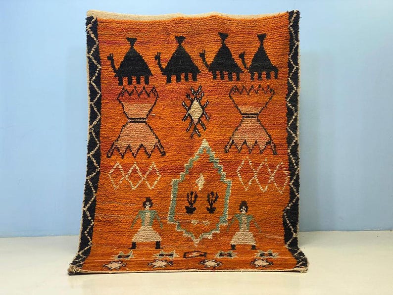 a vibrant, intricately designed rug with a striking orange and black color scheme. The rug is adorned with various geometric patterns and figures, including people and animals, creating a visually captivating and culturally rich design.