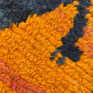 The image is a close-up of a vibrant, textured fabric with a striking pattern of orange and black hues.