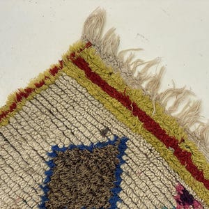 a close-up view of a colorful, textured rug with a fringed edge and a geometric pattern.